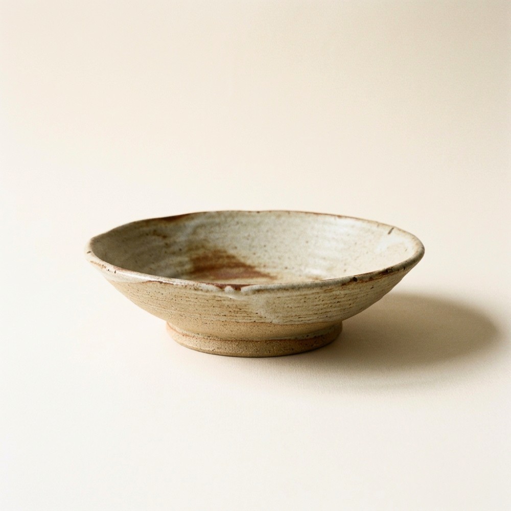 A wide shallow stoneware serving bowl with a pale ash glaze pooling in the well and a raw clay foot ring.