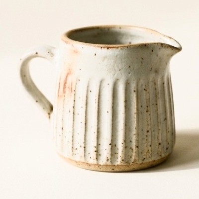 A small fluted stoneware milk jug with a pinched spout.
